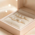 Bijou symbolique naissance baptême : bien le choisir Bijoux délicats pour bébé posés dans un élégant écrin, éclairage doux et lumineux, détails fins brillants sur un tissu satin avec arrière-plan légèrement flou.